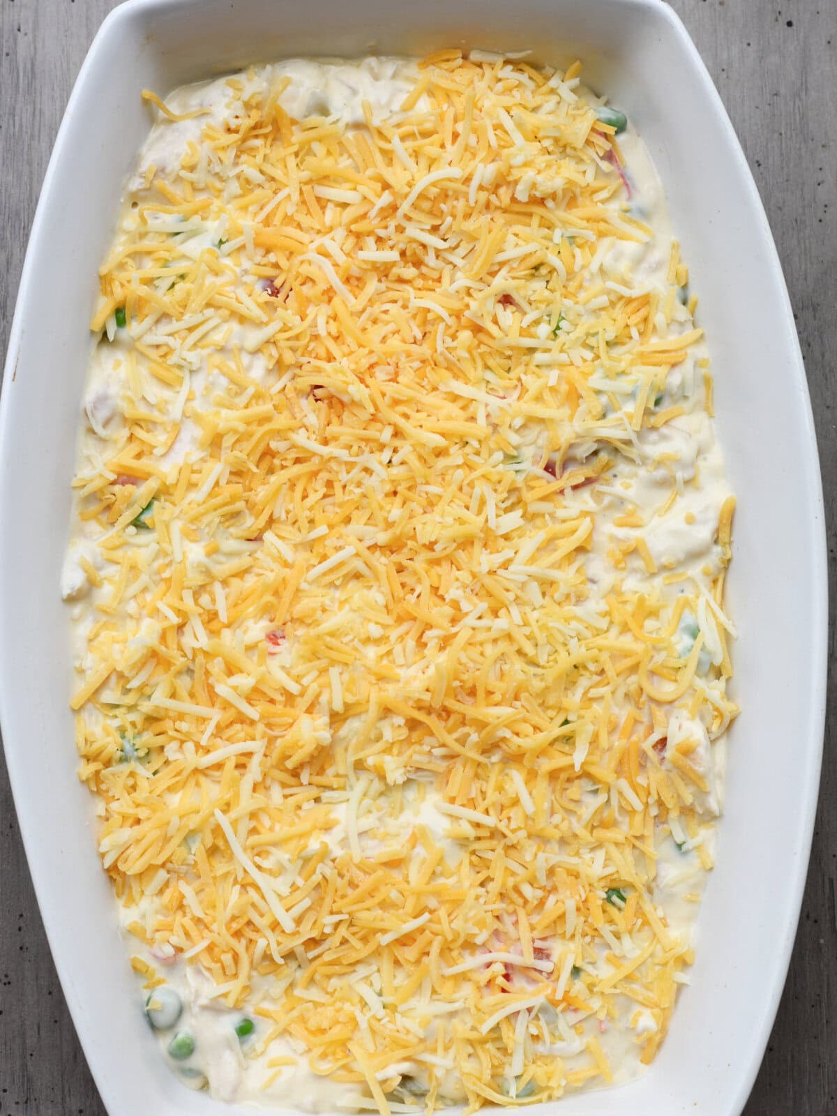 A greased baking dish with cheese sprinkled over a unbaked casserole. 