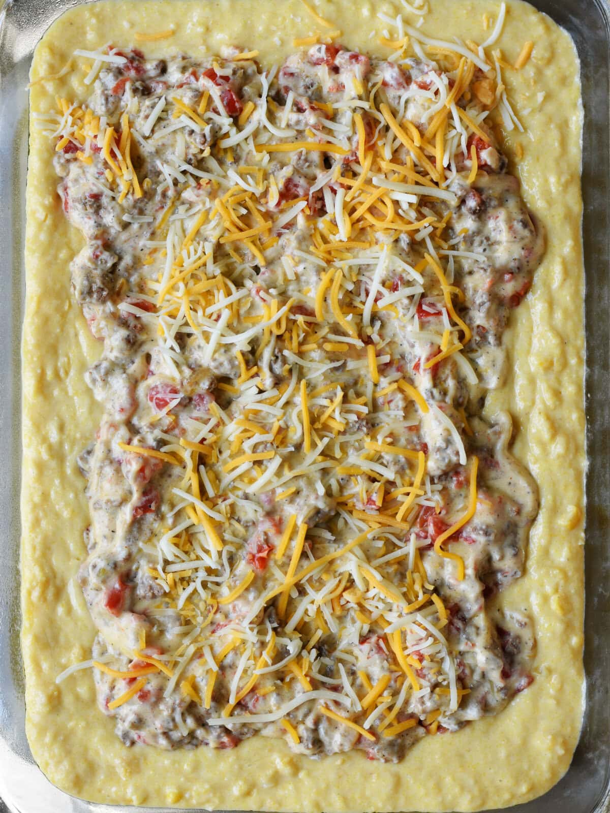 Jiffy corn muffin mix uncooked in a 9X13 glass pan with a creamy ground beef mixture on top. 