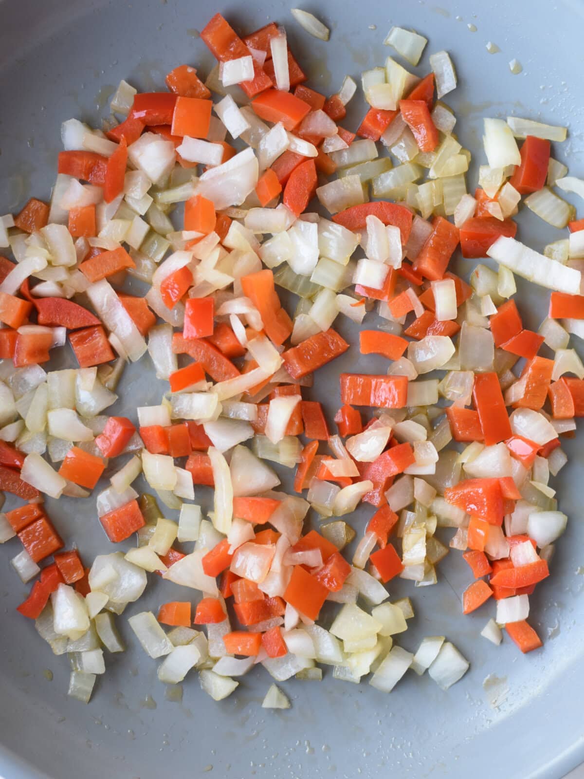 Onions, olive oil and red peppers in a pan searing on the oven. 