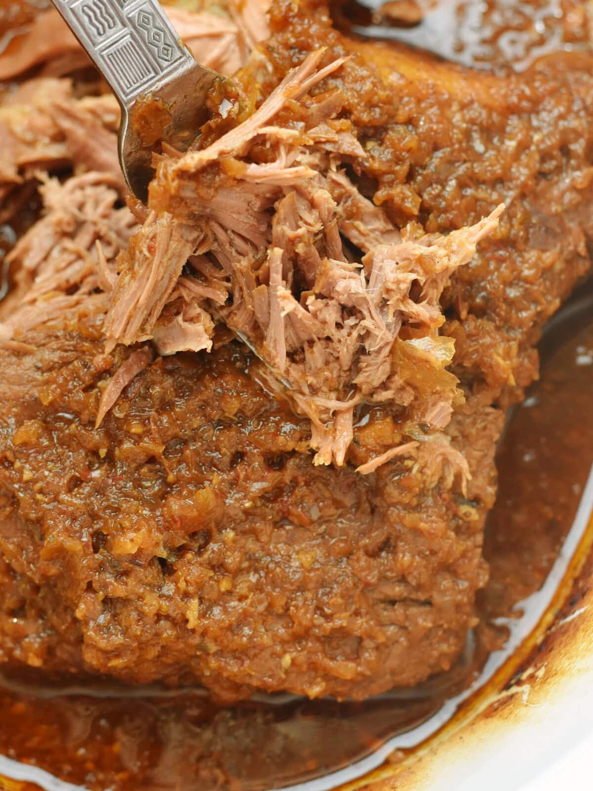 Pulling beef with forks in a crock pot and mixing it with the juices. 