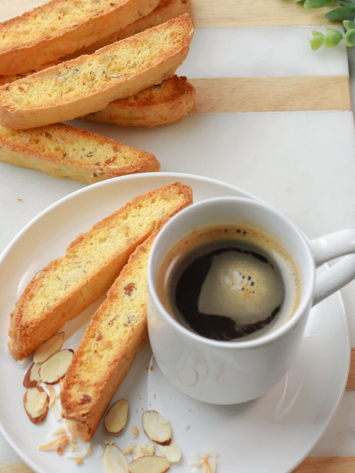 Two slices of Almond Biscotti made with dried fruit and coconut beside a cup of coffee with sliced almonds beside it. 