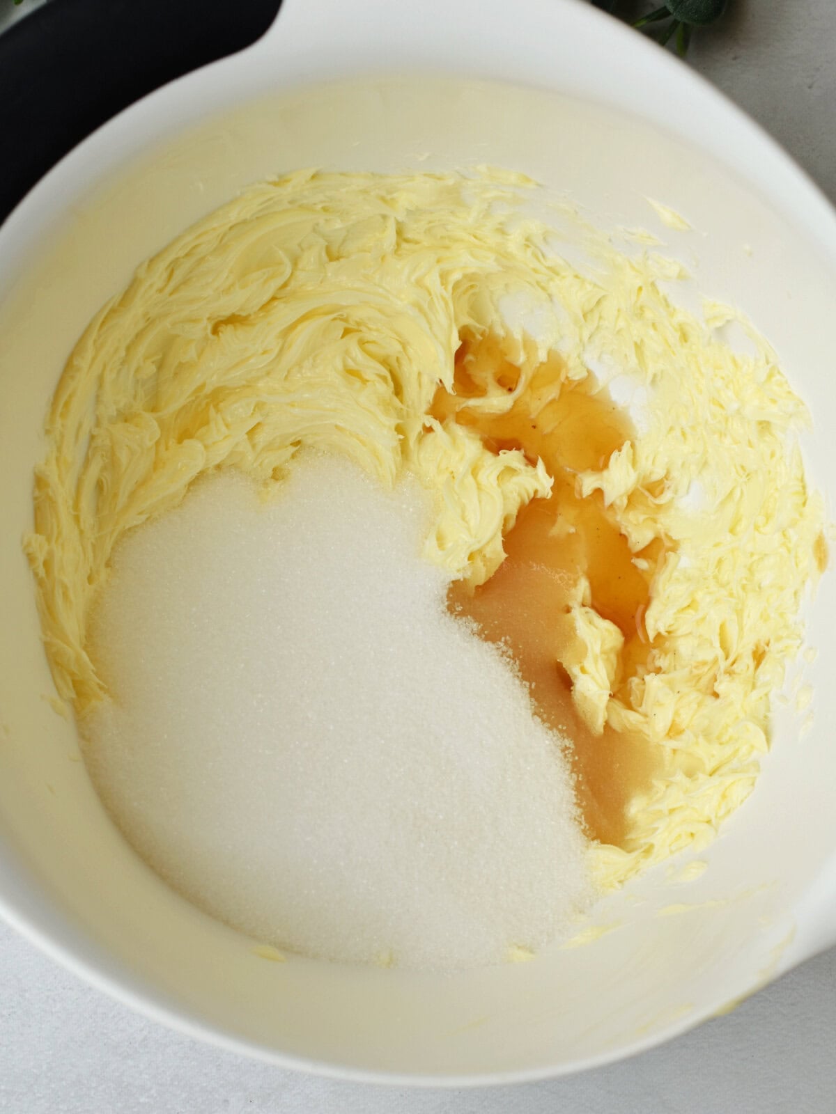 Butter, sugar and vanilla extract in a white mixing bowl. 