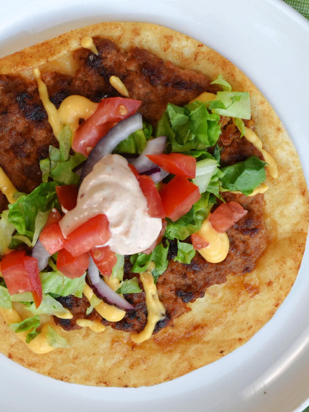 Smash Burger Tacos with Pork on a white plate garnished with lettuce, onions, tomatoes and chipotle sauce. 