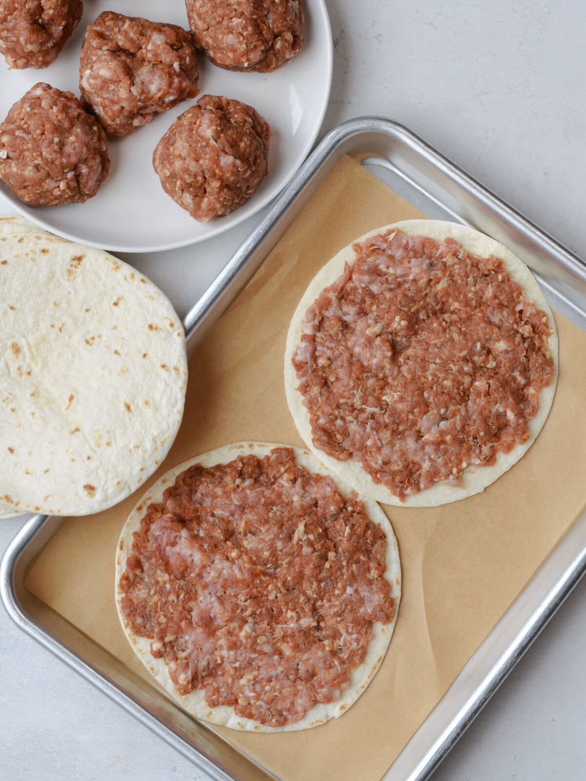 Raw ground meat on a tortilla on a baking sheet. 
